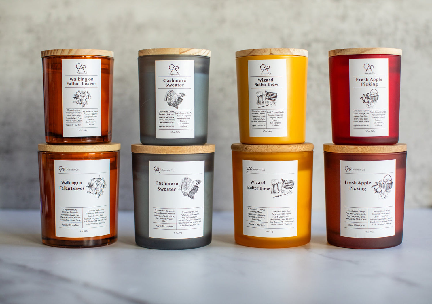 Colorful Frosted Glass Scented Candles lined up neatly showing 2 sizes and multiple scents featured in the Autumn Collection on a beautiful white marble and stone background