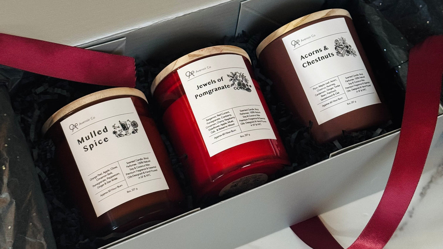 Three candles in a gift box with a red ribbon on a marble surface.