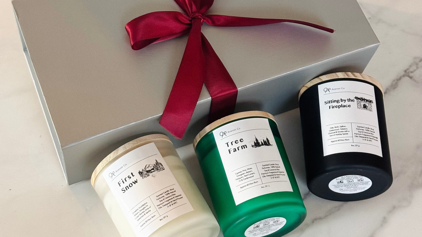 Three candles in different colors with labels, tied together by a red ribbon, on a marble surface.