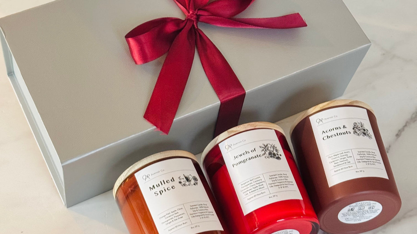 Three candles in a gift box with a red ribbon on a marble surface.