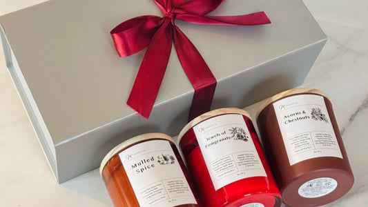 Three candles in a gift box with a red ribbon on a marble surface.